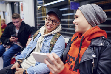 Junges Paar wartet in einer U-Bahn-Station und schaut auf sein Smartphone - CUF07492