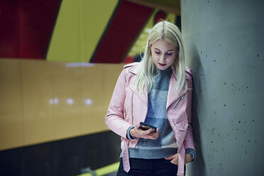 Junge Frau wartet in einer U-Bahn-Station und schaut auf ihr Smartphone - CUF07493