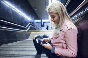 Young woman sitting on underground station stairway looking at smartphone - CUF07498