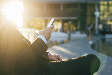 Mature businessman sitting outdoors, using smartphone, mid section - CUF07501