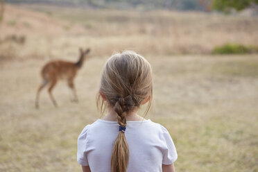 Girl in rural setting, watching mountain reedbuck antelope, rear view - CUF07513