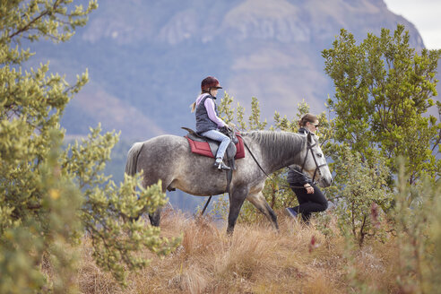Mädchen reitet auf einem Pferd in ländlicher Umgebung, Mutter geht an ihrer Seite - CUF07515
