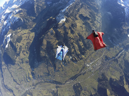Luftaufnahme von zwei Wingsuit-Fliegern, einer auf dem Rücken, der andere im roten Anzug fliegt über die Landschaft - CUF07525