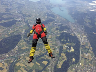 Fallschirmspringerin im freien Fall auf dem Rücken über der Landschaft - CUF07526