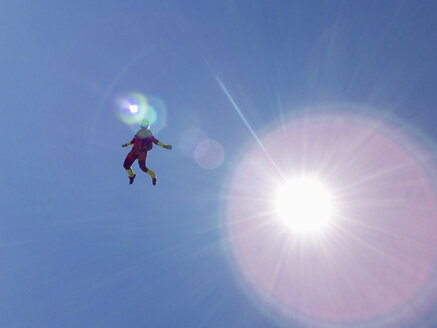 Weiblicher Fallschirmspringer im freien Fall aufrecht gegen den sonnenbeschienenen blauen Himmel - CUF07527