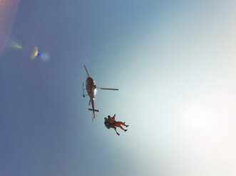 Low angle view of tandem skydiving jump from a helicopter against sunlit blue sky - CUF07529