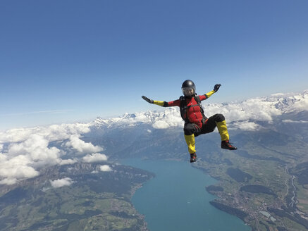 Fallschirmspringerin sitzend im freien Fall über Wolken und See - CUF07531