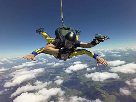 Porträt von Tandem-Fallschirmspringern im freien Fall über Wolken und Landschaft - CUF07532