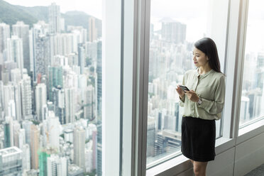 Geschäftsfrau mit Smartphone schaut aus dem Fenster - CUF07665