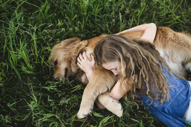 Draufsicht auf ein im Gras liegendes Mädchen, das einen Golden Retriever Hund umarmt - CUF07669