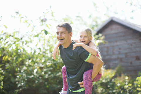 Vater nimmt Tochter im Garten huckepack, lizenzfreies Stockfoto