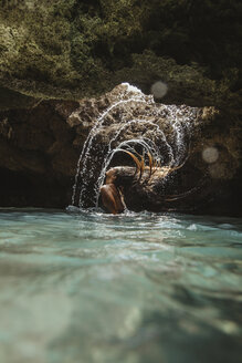 Woman in water filled cave throwing back wet hair, splashing, Oahu, Hawaii, USA - ISF01464