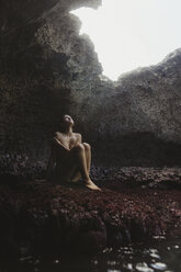 Junge Frau sitzt auf Felsen und schaut aus einer Höhle, Mermaid Caves, Oahu, Hawaii, USA - ISF01470