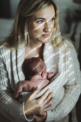 Porträt einer erwachsenen Frau, die ihre neugeborene Tochter in eine Strickjacke gewickelt in den Arm nimmt - ISF01495
