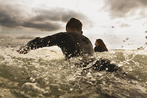 Zwei Freunde im Meer, paddelnd auf Surfbrettern, Rückansicht, lizenzfreies Stockfoto