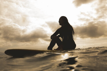 Side view of young woman sitting on surfboard in sea against