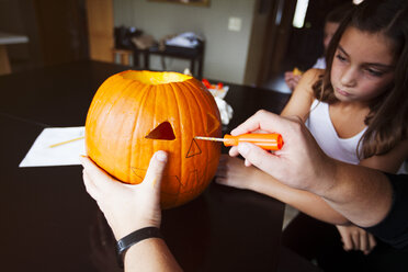 Daughter watching father carve pumpkin - ISF01527