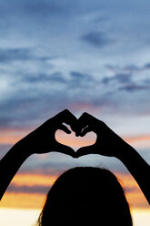 Silhouette of girl making heart with her hands against dramatic sky - ISF01555