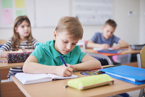 Schoolboy writing in exercise book in class - ABIF00368