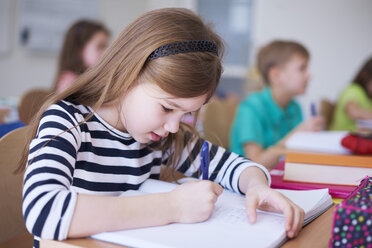 Schoolgirl writing in exercise book in class - ABIF00370