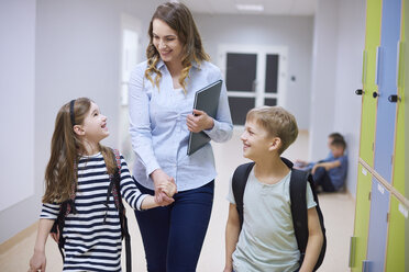 Lächelnde Schüler und Lehrer gehen Hand in Hand auf dem Korridor in der Schule - ABIF00384