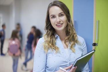 Porträt eines lächelnden Lehrers auf einem Schulflur mit Schülern im Hintergrund - ABIF00391