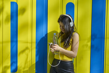 Junge Frau, die mit Kopfhörern und Wasserflasche Musik hört und Textnachrichten schreibt - BEF00066