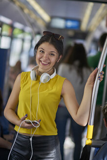 Porträt einer lächelnden jungen Frau mit Handy und Kopfhörern in einem U-Bahn-Zug - BEF00068