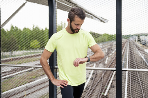 Mann, der eine Pause vom Laufen macht und die Zeit auf einer Smartwatch überprüft, lizenzfreies Stockfoto