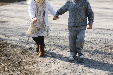 Geschwister halten sich an den Händen und gehen auf einer Schotterstraße - ISF01560