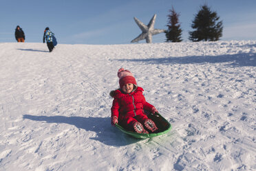 Girl in red knit hat tobogganing down snow covered hill - ISF01571