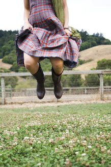 Blick von unten auf eine Frau im karierten Kleid, die mitten in der Luft auf einem Feld springt - ISF01586