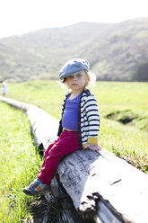 Porträt eines männlichen Kleinkindes mit flacher Mütze auf einem Baumstamm sitzend - ISF01591