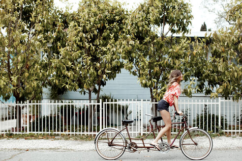 Young woman cycling alone on tandem bicycle along street - ISF01599