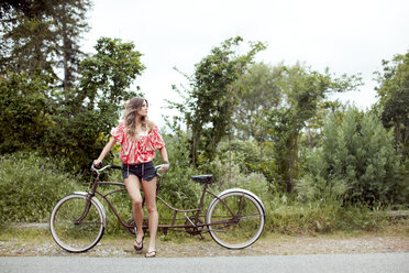 Young woman with tandem bicycle looking over her shoulder on rural road - ISF01601
