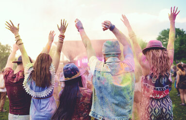 Rear view of young adult friends dancing and throwing coloured chalk powder at festival - ISF01654