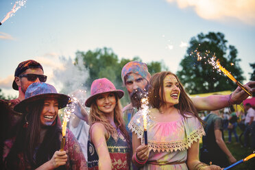 Young adults covered in coloured chalk powder dancing with sparklers at festival - ISF01661