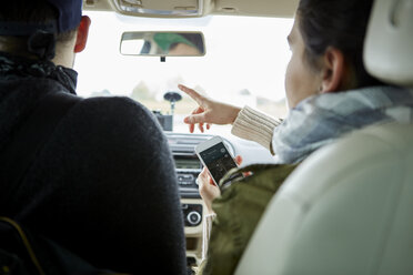 Junges Paar sitzt im Auto, Frau hält Smartphone, zeigt Richtungen, Rückansicht - ISF01675