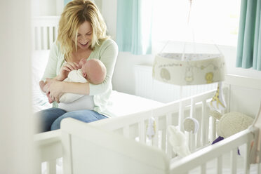 Mother sitting on bed, holding newborn baby - CUF07735