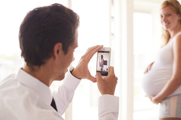 Over shoulder view of man taking smartphone photograph of pregnant girlfriend - CUF07753