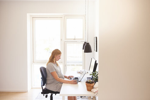 Pregnant young woman at desk typing on laptop - CUF07772