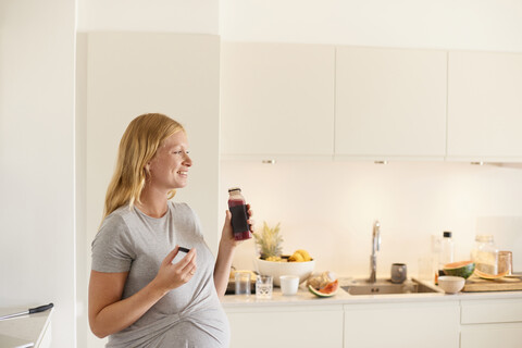 Schwangere junge Frau in der Küche mit einer Flasche Fruchtsaft, lizenzfreies Stockfoto