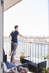 Mid adult man looking out from waterfront apartment balcony - CUF07782