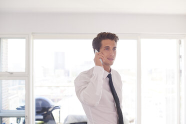 Businessman in living room making smartphone call - CUF07787