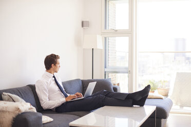 Businessman sitting on sofa using laptop - CUF07789