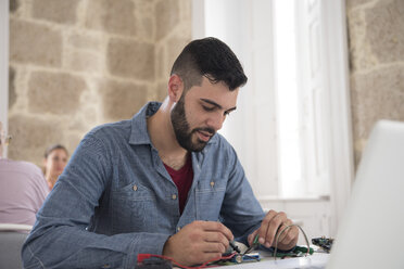 Young male computer technician repairing cable on office desk - CUF07794