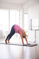 Schwangere junge Frau beugt sich nach vorne und macht Yoga-Übungen im Wohnzimmer - CUF07814