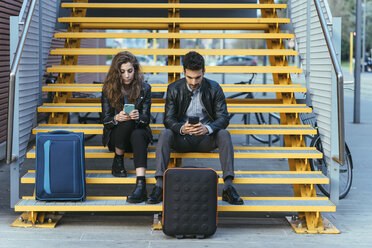Couple with luggage, using mobile phone on steps, Florence, Italy - CUF07865