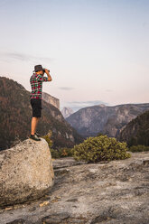 Mann steht auf einem Felsen und schaut durch ein Fernglas, Yosemite National Park, Kalifornien, USA - CUF07873