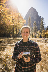 Portrait of woman holding camera in autumn landscape, Yosemite National Park, California, USA - CUF07875